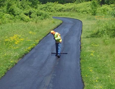 employee smoothing out fresh asphalt on a path